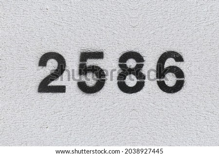 Black Number 2586 on the white wall. Spray paint. Number two thousand five hundred and eighty six.