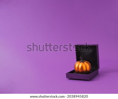 Shiny pumpkin in ring gift box for fun Halloween present concept. Purple and orange.