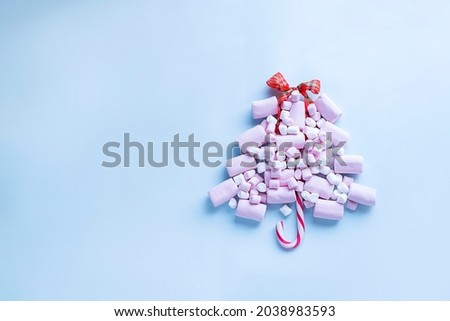Christmas tree made of pink marshmallows and candy cane on light blue background
