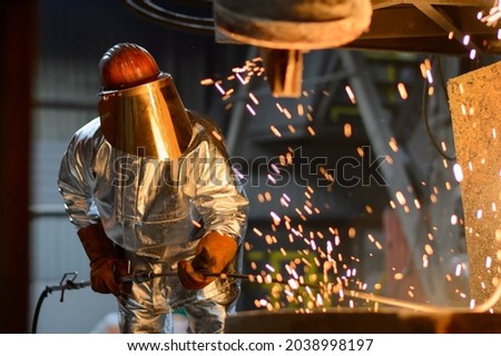 A steelworker when casting draining metal from a cupola furnace. Metallurgy. Royalty-Free Stock Photo #2038998197