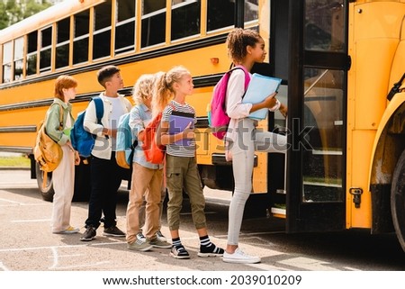Schoolchildren kids pupils group of mixed-race classmates boarding school bus before going to lessons, coming back to school, standing in line. New educational year semester. Royalty-Free Stock Photo #2039010209