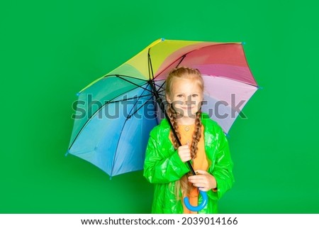 a child girl on an isolated green background with an umbrella and a raincoat smiles, space for text
