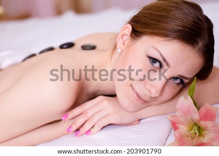 picture in spa: attractive lady having fun enjoying relaxation during stone therapy massage & aromatherapy happy smiling & looking at camera lying on white bed copy space background closeup portrait