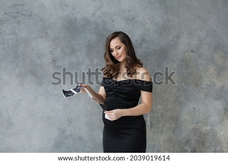 Pregnant woman looking at ultrasound scan image on gray background