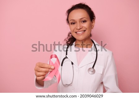 Beautiful African American female doctor with beautiful toothy smile showing a Pink satin Ribbon, isolated on colored background with copy space. World Day of fight Breast Cancer, 1 st October concept Royalty-Free Stock Photo #2039046029