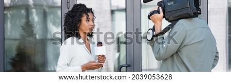 brunette african american journalist doing reportage near cameraman outside, banner Royalty-Free Stock Photo #2039053628