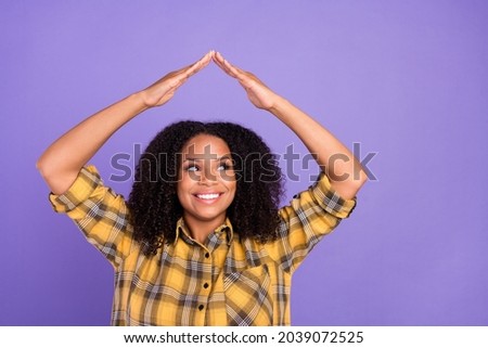 Photo of dreamy happy afro american woman look empty space hands roof above head isolated on purple color background
