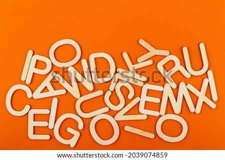 Wooden alphabet letters on orange paper background. A lot of wooden letters with copy space.