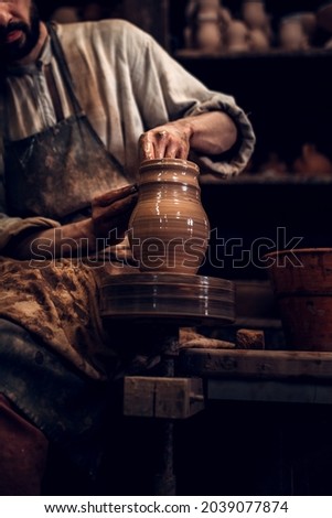 A master potter in an old craft workshop professionally forms a pot of clay with his hands Royalty-Free Stock Photo #2039077874