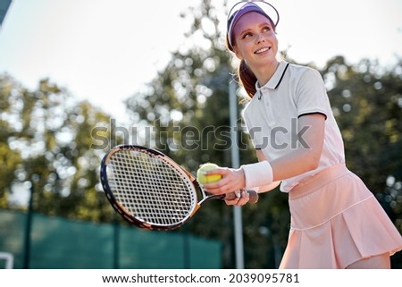 Woman in sportswear playing tennis. Tournament. Fit caucasian Sportswoman in skirt looking at side, going to throw ball to opposer holding racket in hands. At summer day in court. Tennis concept