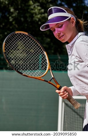 Beautiful Young Caucasian Lady In White Uniform And Cap Holding Tennis Racket In Hands, Smiling, Motivated Sportswoman On Hardcourt At Summer Day. People Lifestyle, Fitness, Sport Concept