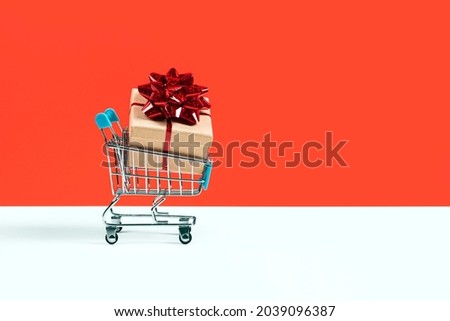 Toy shopping cart or trolley with large gift box. A gift for a holiday, anniversary, or birthday. Trolley cart with a gift box Isolated over red background. Banner with copy space.