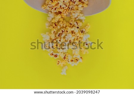 At the top of the photo is an inverted white popcorn box, popcorn spills out of it on a yellow background. top view, flat lay, copy space, isolate