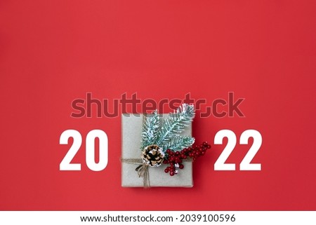 Present box decorated with mistletoe, pine cone and numbers 2022 on red background. Minimal concept of Christmas gift. Flat lay, top view, copy space