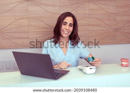 young woman working at the reception of a dental office charges patient services with a credit card