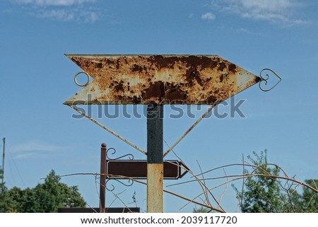 one old gray metal arrow signpost in brown rust on the street against the blue sky