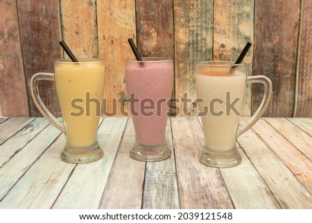 Vanilla, strawberry and mango smoothies served in glass jars with black straws on wooden table