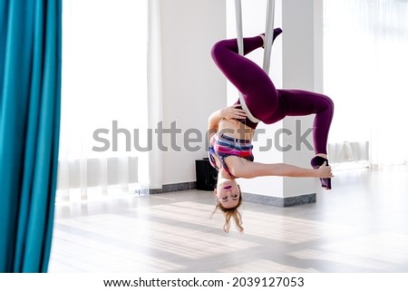 Beautiful young woman Hanging upside down by hammock for doing pose of anti-gravity yoga in yoga studio. 