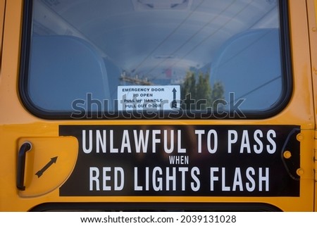 Rear view of a school bus. Closeup of the emergency door with a warning sign which reminds people of the rule that it is unlawful to pass when red lights flash.