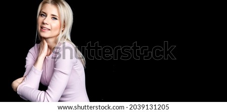 BLOND SMILING MODEL GIRL WITH BLUE EYES ON BLACK BACKGROUND SITTING PINK BLOUSE BLUE JEANS