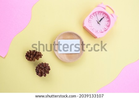 Business Card On Wood With Pine Flowers And Alarm Clock On Yellow And Pink Background. minimalist style
