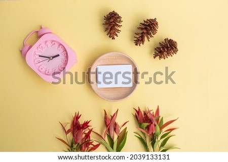 Business Card On Wood With Pine Tree Flowers and Alarm Clock On Pastel Yellow Background. minimalist style

