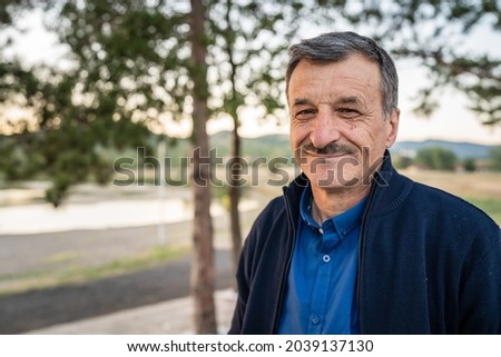 Portrait of senior caucasian man in nature standing in spring or autumn day - close up of cheerful male standing looking to the camera - real people concept