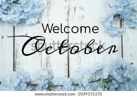 Welcome October text and blue flower decoration on wooden background
