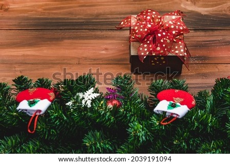 Gift box with red color ribbon on wood background with Christmas tree and traditional ornaments Xmas props with copy space. Concept of happy and joyful in festival.