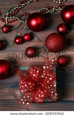 Close up shot of gift present box wrapped with golden ribbon bow placed on old dark wooden table in front glossy shiny decorative hanging balls and star in blurred background with copy space.