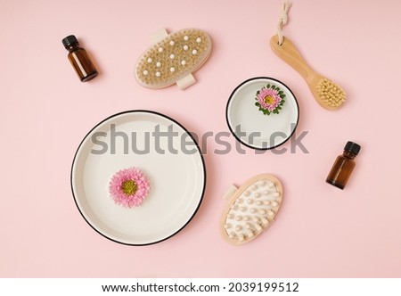 Pink and violet chrysanthemum flower buds floating in white round bowls with water and beauty cosmetic accessories on a pink background. Minimal natural flat lay. Eco friendly wellness products. 