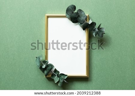 Empty photo frame with eucalyptus leaf on green background. top view, copy space