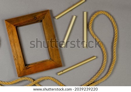 Empty photo frame and rope against a gray background. Wooden picture frame. Natural rope. Group of aluminum tubes. Top view.