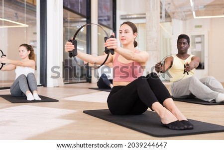 Positive young woman practicing pilates with ring at group class in yoga studio