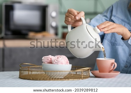 Woman pouring aromatic tea from teapot into cup in kitchen Royalty-Free Stock Photo #2039289812