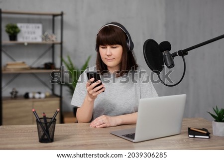 young woman recording a podcast using smartphone, laptop, microphone and headphones in home studio