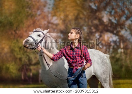 a beautiful girl rider is engaged with a white horse on the background of autumn trees