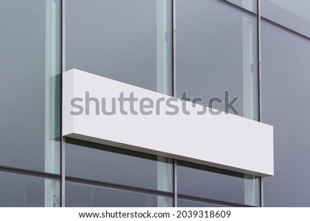 Long white shop banner sign board hanging on glass office building surface.