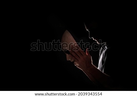 Backlight of a man wearing a mask. Concept of hiding and mystery. Silhouette. Image halloween. Black background with space for copying.