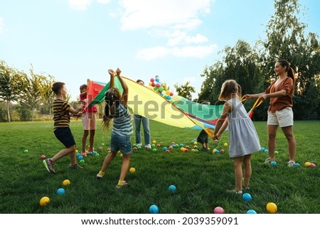 Group of children and teacher playing with rainbow playground parachute on green grass. Summer camp activity Royalty-Free Stock Photo #2039359091