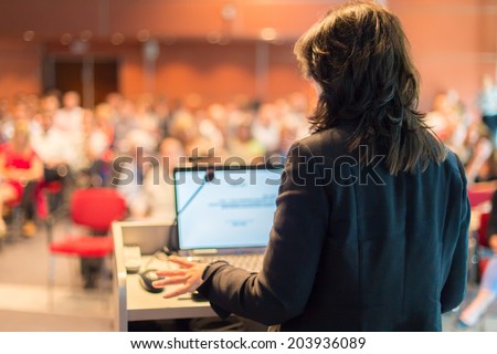 Business woman lecturing at Conference. Audience at the lecture hall.