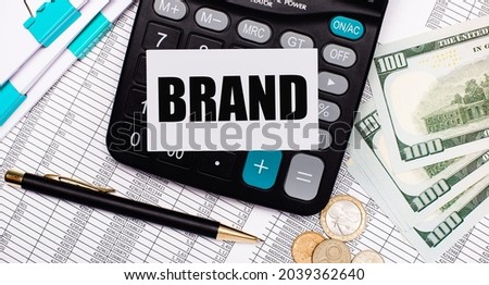 On the desktop are reports, a pen, cash, a calculator and a card with the text BRAND. Business concept