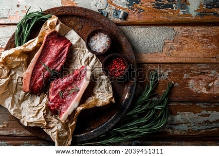  Raw marbled beef steaks and seasonings for their preparation on the old wooden background, top view, copy space for text. Raw beef meat on the kitchen table. High quality photo