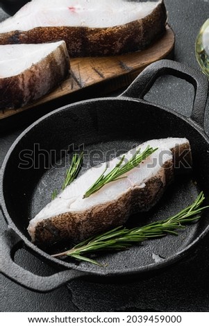 Raw fresh halibut fish steak set, with ingredients and rosemary herbs, on black dark stone table background