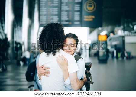 Young family couple at the airport departure area saying goodbye or hello, embracing each other with smile. Arrival and reunion awaiting after travel Royalty-Free Stock Photo #2039461331