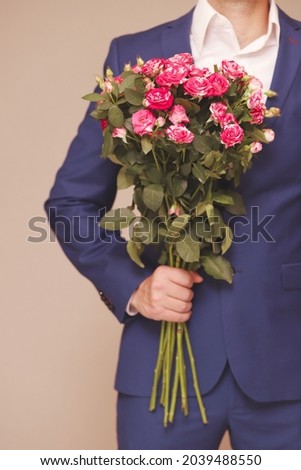 A young man in a blue suit with a beautiful bouquet of roses in his hand. Selective focus. Concept: a gift for a woman on a holiday. Vertical photo