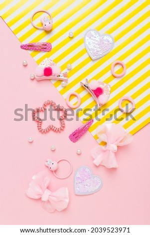 Cute girl's hair accsessories on pink and yellow striped background. Hair clips, hairpins, bow tie on pink background. Fashion hair accessories for little girls. Flat lay. Place for text.