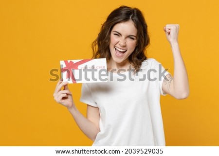 Young happy overjoyed fun caucasian woman in white basic t-shirt point index finger on gift voucher flyer mock up do winner gesture clench fist celebrate isolated on yellow background studio portrait