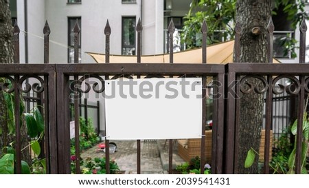 Empty white name plate with space for mockup hangs on metal house gate outside
