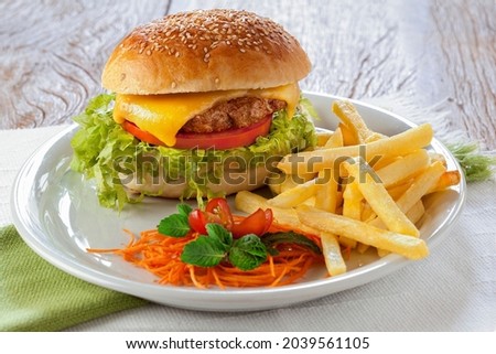 Tasty hamburger with french fries on plate on rustic table.